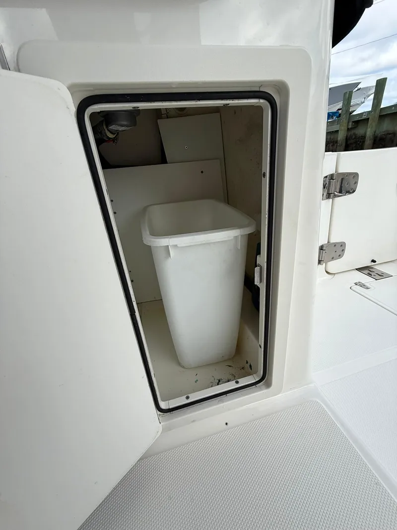 Slide: The Image of 2020 Boston Whaler 325 Conquest storage compartment with a white trash bin inside. - 12