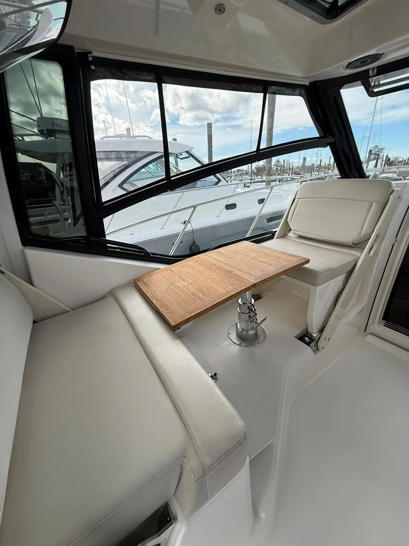 Slide: The Image of 2020 Boston Whaler 325 Conquest interior with seating and wooden table, docked at marina. - 15