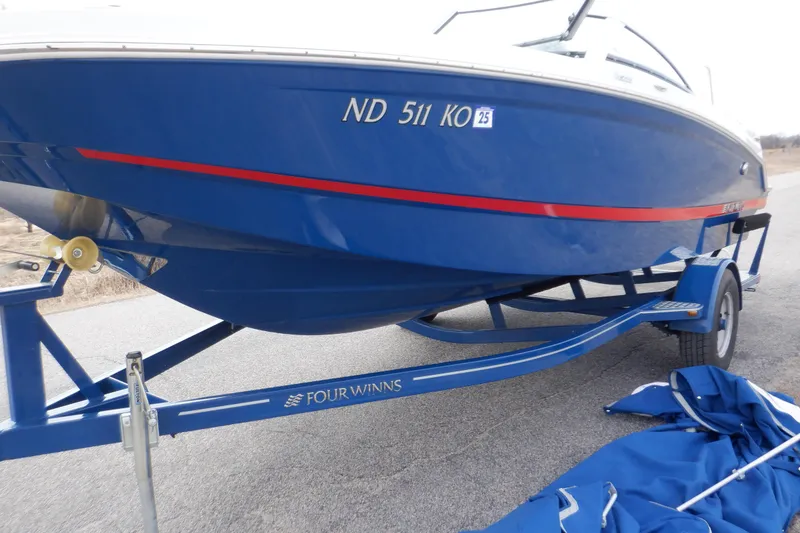 Slide: The Image of 2018 Four Winns HD200 boat on trailer, blue hull with red stripe, parked on road. - 14