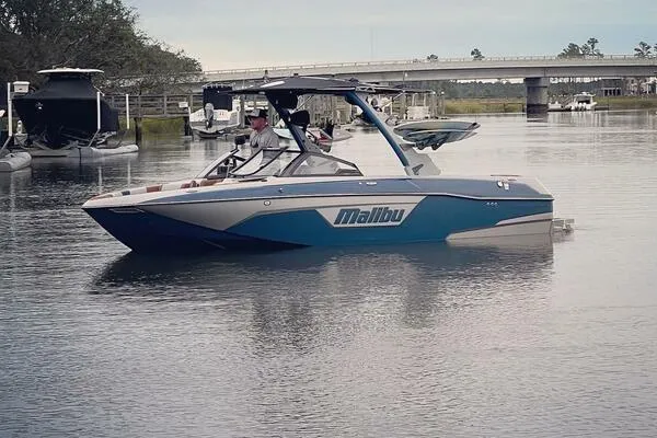 Slide: The Image of 2023 Malibu Wakesetter 23 LSV boat on calm water near a bridge. - 2