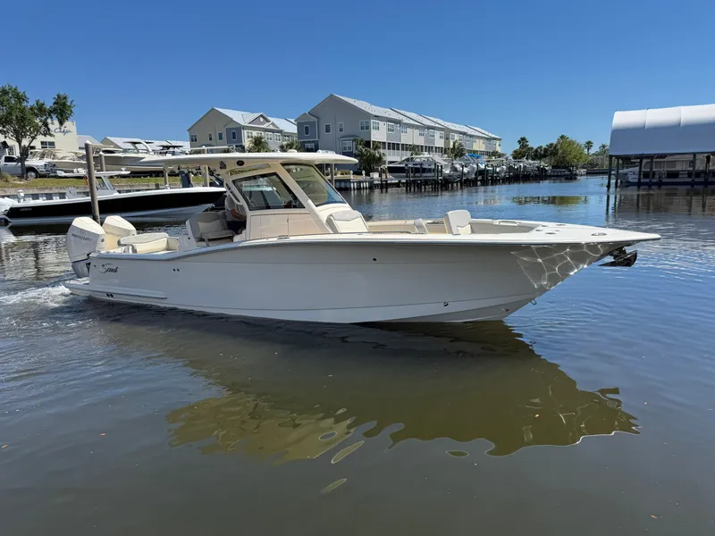 Slide: The Image of 2023 Scout 305 LXF boat cruising on a calm waterfront near residential docks. - 5
