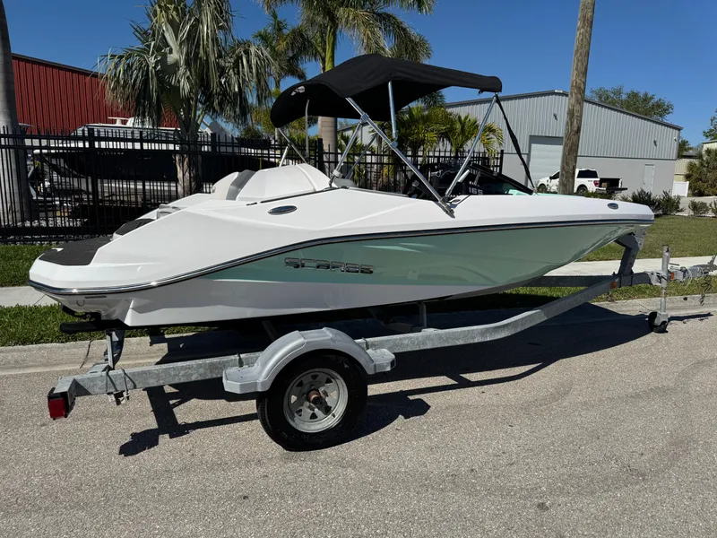 Slide: The Image of 2022 Scarab 165 ID boat on trailer, parked outdoors with palm trees in background. - 2
