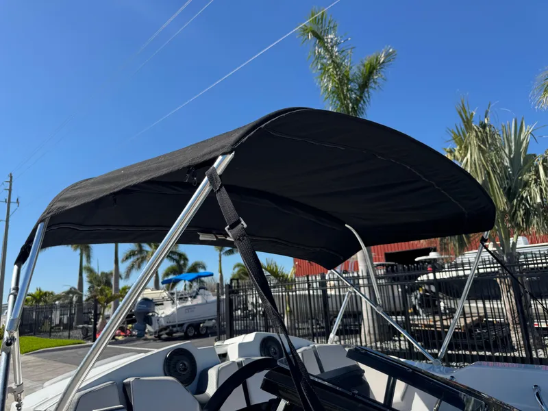 Slide: The Image of 2022 Scarab 165 ID boat with black canopy, parked near palm trees under a clear blue sky. - 31