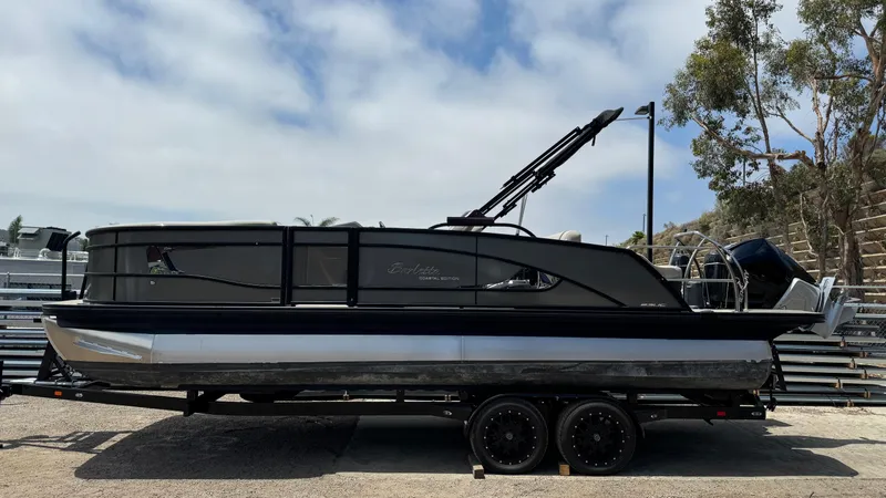 Slide: The Image of 2023 Barletta Lusso 23UC pontoon boat on a trailer, parked outdoors. - 3