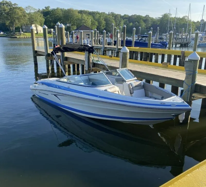 Slide: The Image of 2023 Crownline 240 SS boat docked at a marina, surrounded by calm water and greenery. - 1