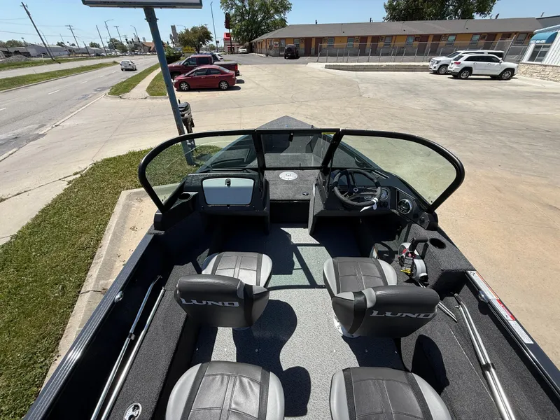 Slide: The Image of 2025 Lund 1650 Rebel XL Sport boat interior with seating and dashboard, parked outdoors. - 5