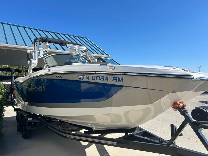 Slide: The Image of 2020 MasterCraft X24 boat on trailer, blue and white, parked under a metal roof. - 3