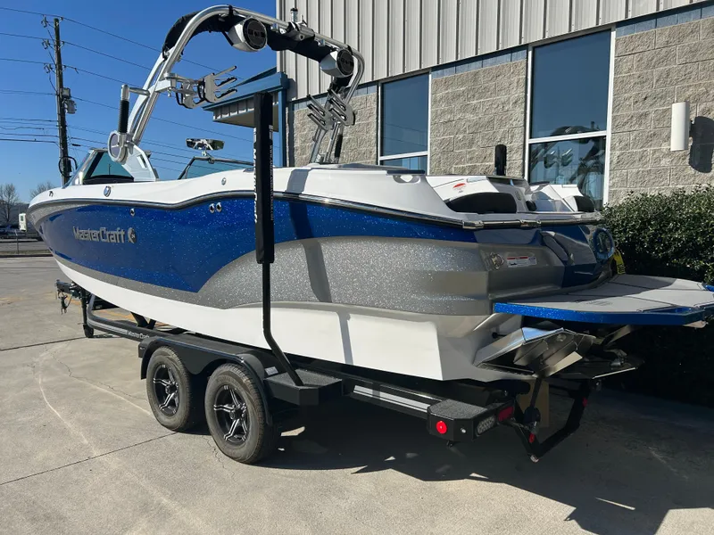 Slide: The Image of 2020 MasterCraft X24 boat on trailer, blue and white, parked outside a building. - 4