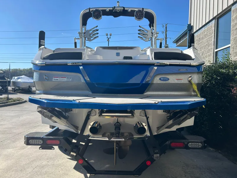 Slide: The Image of 2020 MasterCraft X24 boat, rear view, blue and white, parked outdoors. - 5