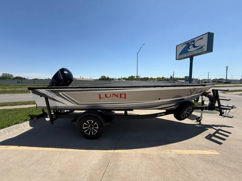 Slide: The Image of 2025 Lund 1875 Pro Guide boat on trailer, parked outdoors near dealership sign. - 2