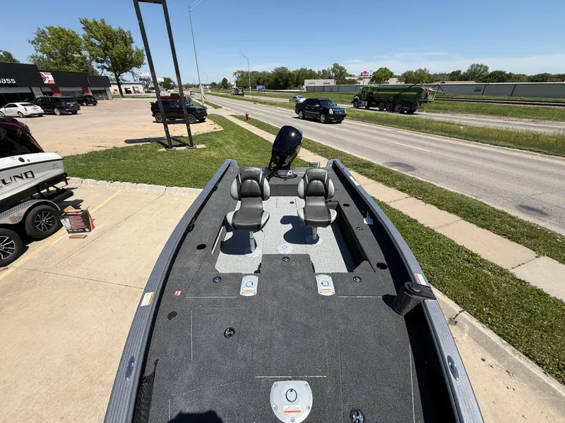 Slide: The Image of 2025 Lund 1875 Pro Guide boat on display, featuring dual seats and a motor, parked near a road. - 5