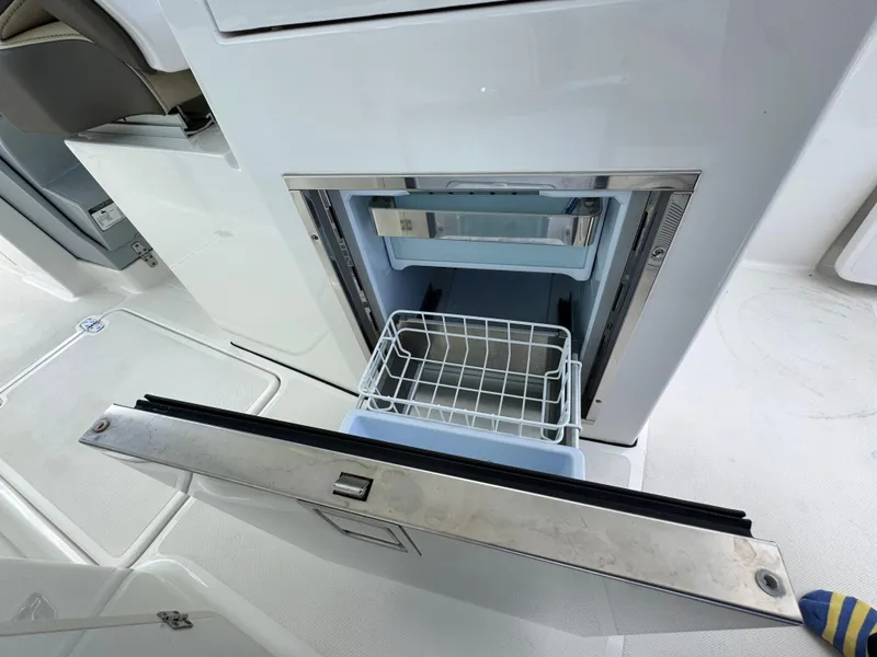 Slide: The Image of Open refrigerator on 2019 Pursuit DC 325 Dual Console boat, showing interior storage. - 18