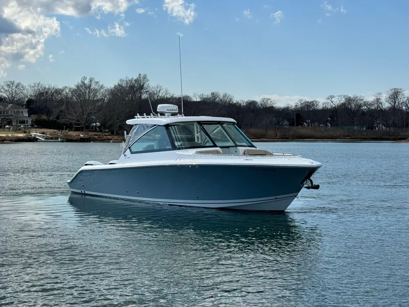Slide: The Image of 2019 Pursuit DC 325 Dual Console boat on calm water under a partly cloudy sky. - 2
