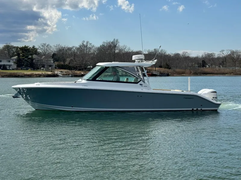 Slide: The Image of 2019 Pursuit DC 325 Dual Console boat on calm water under a partly cloudy sky. - 5