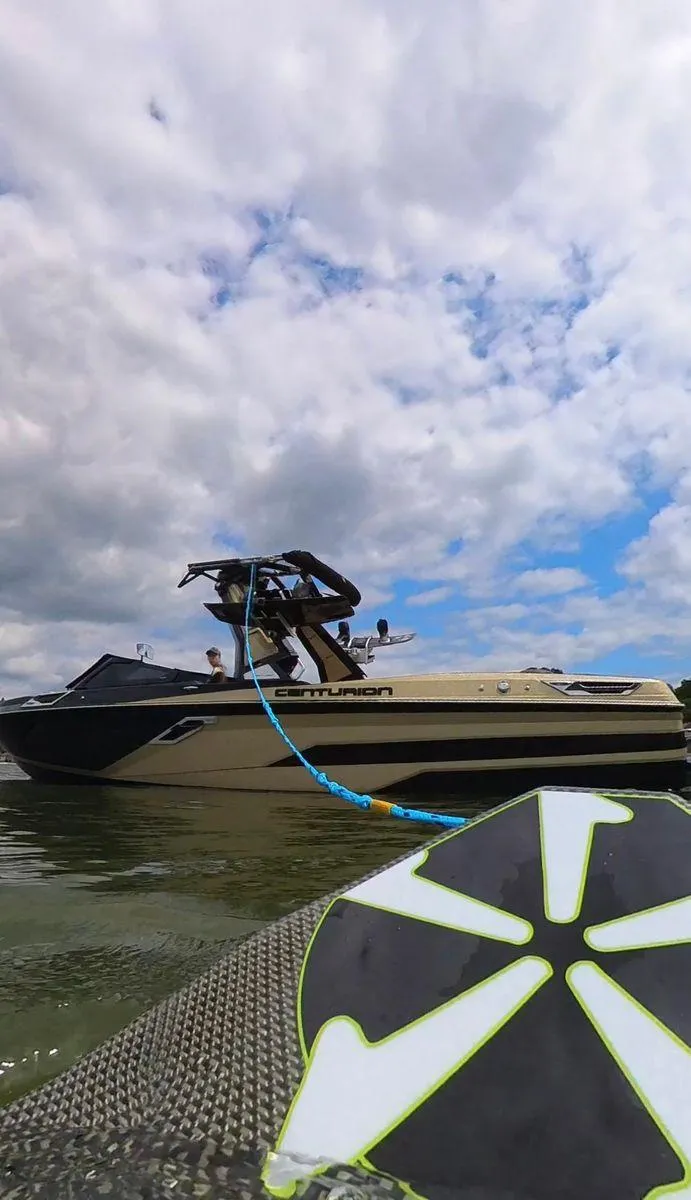 Slide: The Image of 2021 Centurion Ri265 boat on water under cloudy sky, with wakeboard in foreground. - 12