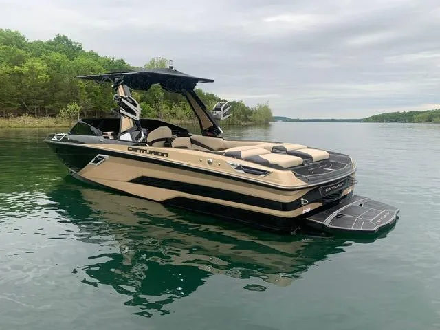 Slide: The Image of 2021 Centurion Ri265 boat on a calm lake with lush green shoreline. - 2