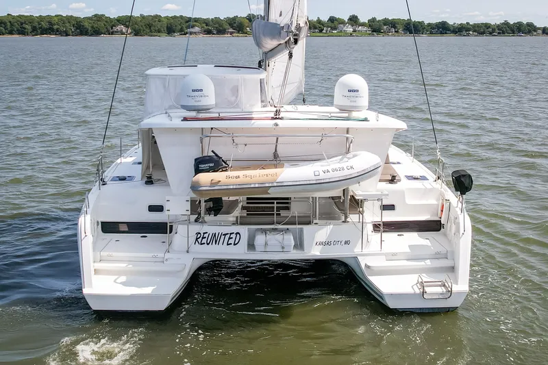 Slide: The Image of 2017 Lagoon 42 catamaran on water, rear view with dinghy and "Reunited" name. - 11