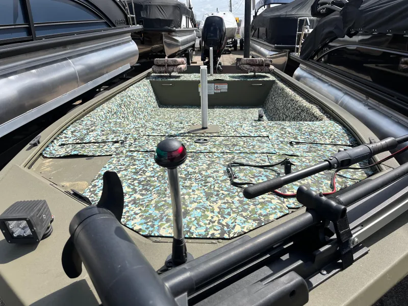 Slide: The Image of 2022 Tracker Grizzly 1648 Jon boat with camouflage interior, docked among other boats. - 3