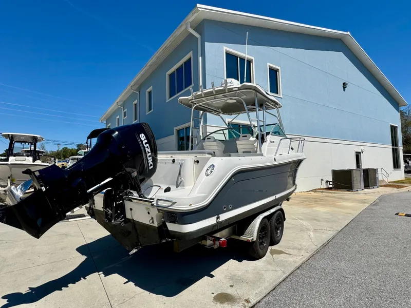 Slide: The Image of 2015 Robalo R245 Walkaround boat with Suzuki outboard motor, parked near a blue building. - 5