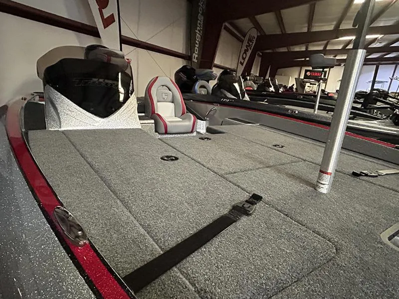 Slide: The Image of 2023 Triton 179 TrX boat interior with gray carpet and red accents in showroom. - 2
