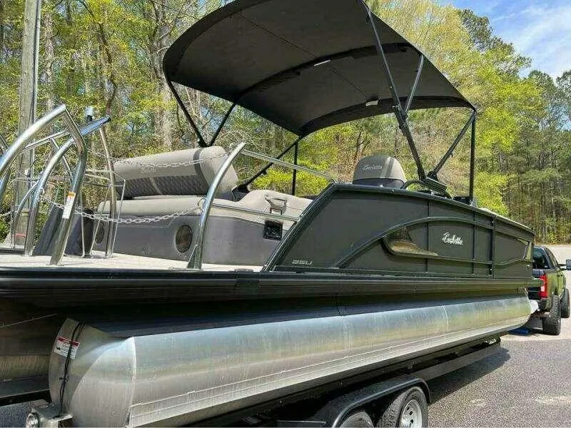 Slide: The Image of 2023 Barletta LUSSO 25U pontoon boat on trailer with canopy, parked outdoors. - 0