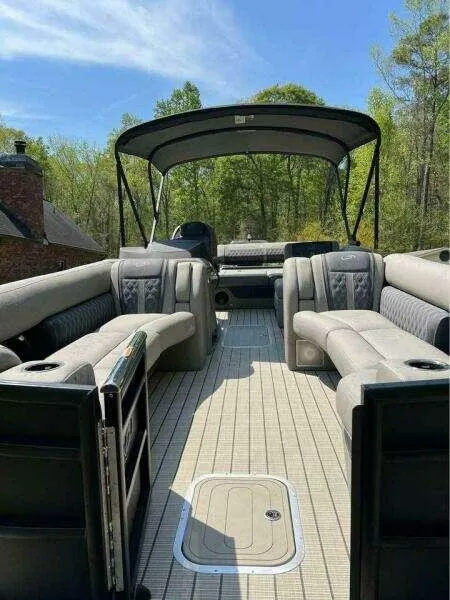 Slide: The Image of 2023 Barletta LUSSO 25U pontoon boat with spacious seating and canopy, set against a wooded backdrop. - 7