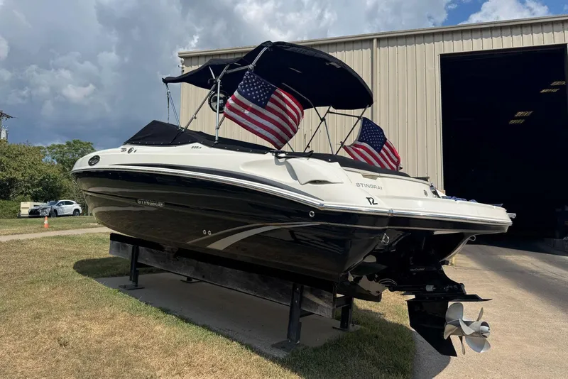 Slide: The Image of 2017 Stingray 235 LR boat with American flags, parked outside a large garage. - 55