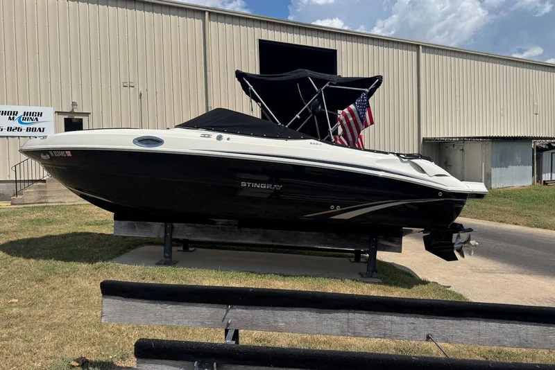 Slide: The Image of 2017 Stingray 235 LR boat displayed outdoors with American flag, near a marina building. - 56