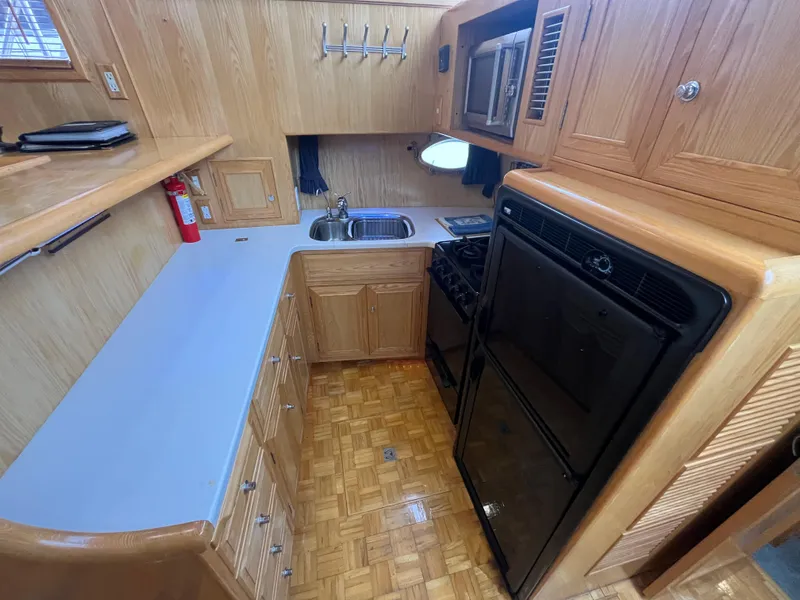 Slide: The Image of 1999 Ocean Alexander Sundeck 460 yacht kitchen with wood cabinetry, stove, sink, and refrigerator. - 23