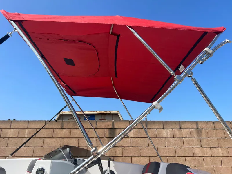 Slide: The Image of Red canopy on 2022 Tahoe T16 boat against blue sky and brick wall. - 17