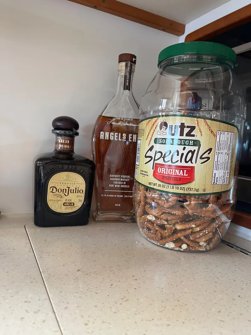 Slide: The Image of Bottles of Don Julio and Angel's Envy beside a jar of Utz pretzels on a countertop. - 26