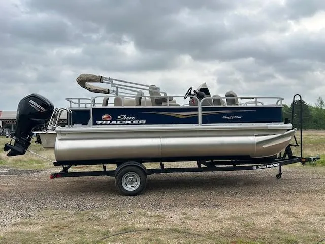 Slide: The Image of 2025 Sun Tracker Bass Buggy 18 DLX pontoon boat on trailer, parked outdoors. - 6
