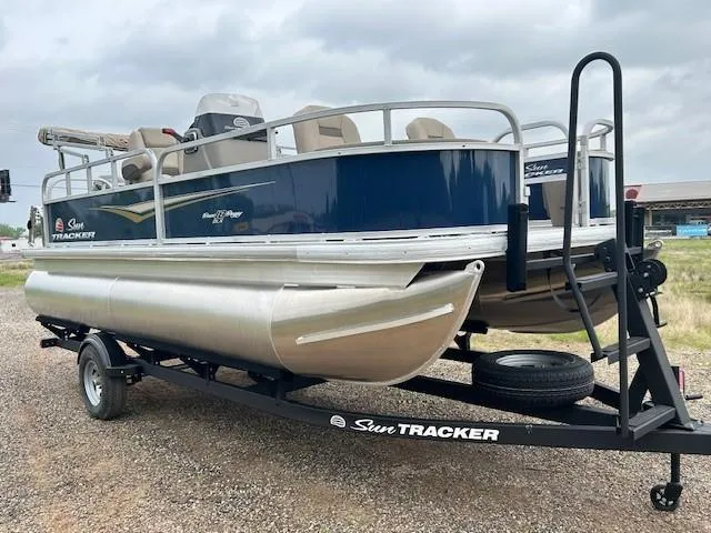 Slide: The Image of 2025 Sun Tracker Bass Buggy 18 DLX pontoon boat on trailer, parked outdoors. - 7