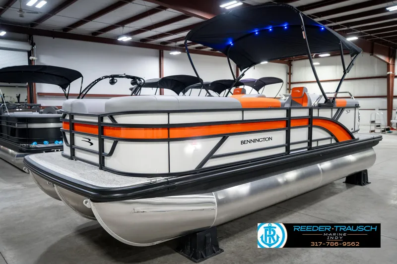Slide: The Image of 2025 Bennington 21 SSR pontoon boat with orange accents in a showroom. - 2