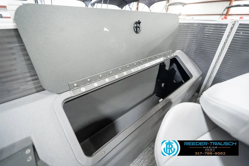 Slide: The Image of 2025 Bennington 21 SS boat storage compartment, open lid, gray interior, Reeder-Trausch Marine logo. - 31