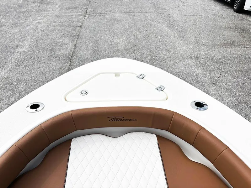 Slide: The Image of 2025 Pioneer 180 Islander boat bow with brown and white seating, docked on pavement. - 11