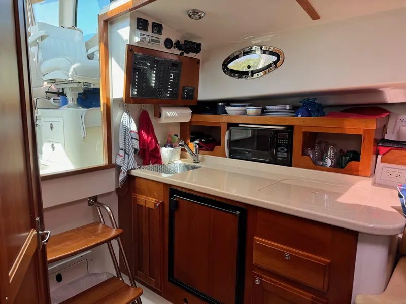 Slide: The Image of 2007 Back Cove 29 yacht interior with kitchenette, featuring sink, microwave, and wooden cabinetry. - 9
