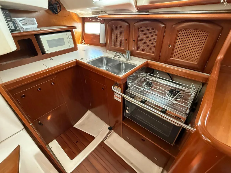 Slide: The Image of 1998 Beneteau Oceanis 352 yacht kitchen with wood cabinetry, dual sink, stove, and microwave. - 17