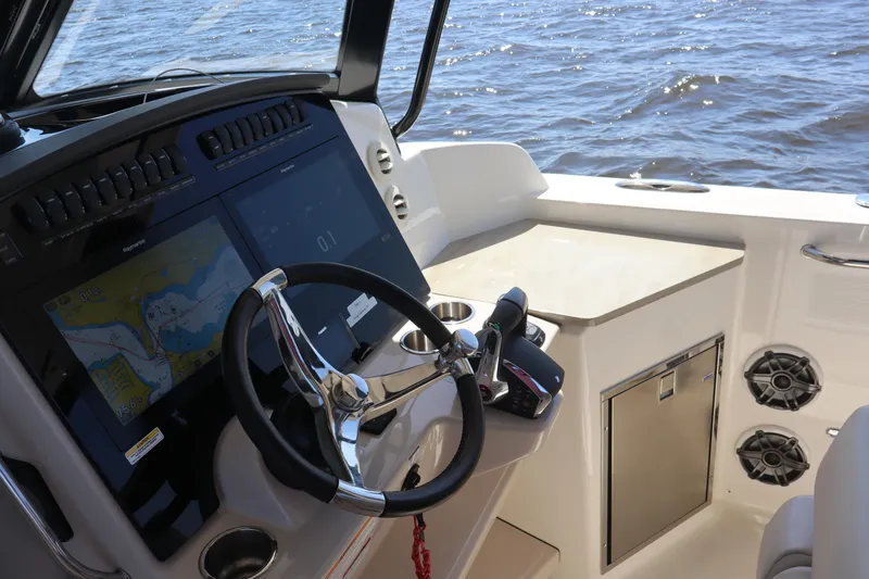 Slide: The Image of 2023 Boston Whaler 350 Realm helm with navigation screens and steering wheel, overlooking the water. - 46
