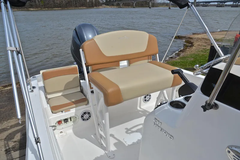 Slide: The Image of 2023 NauticStar 211 Hybrid boat interior with tan seating and console, near a riverbank. - 24