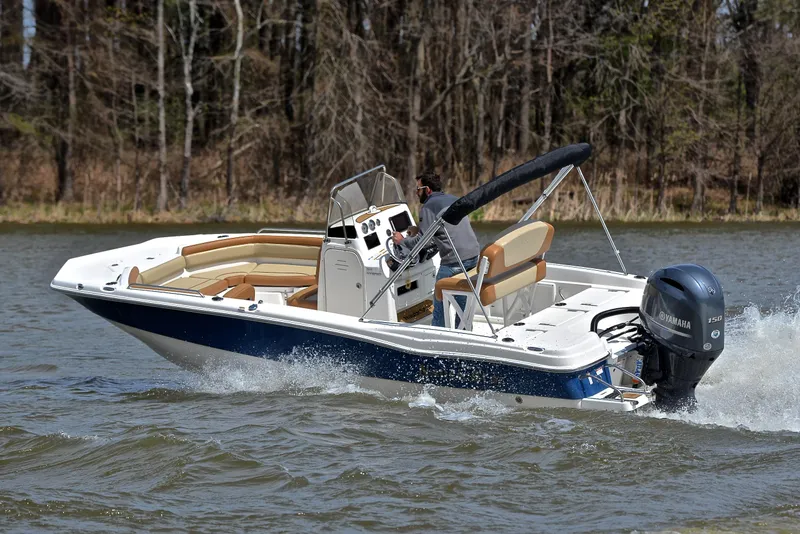Slide: The Image of 2023 NauticStar 211 Hybrid boat cruising on a lake with trees in the background. - 6