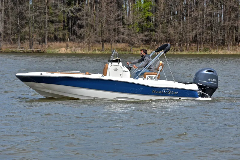 Slide: The Image of 2023 NauticStar 211 Hybrid boat cruising on a lake with a forested background. - 9