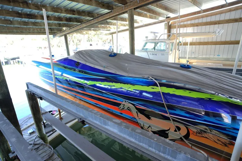 Slide: The Image of 2008 Outerlimits 39 Quattro speedboat with vibrant graphics, docked under a covered structure. - 13