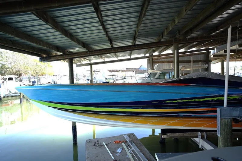 Slide: The Image of 2008 Outerlimits 39 Quattro speedboat with vibrant stripes docked under a covered marina. - 14
