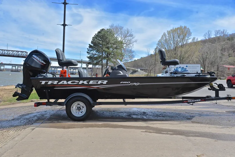 Slide: The Image of 2023 Bass Tracker Pro 170 boat on trailer by riverside, under clear blue sky. - 15