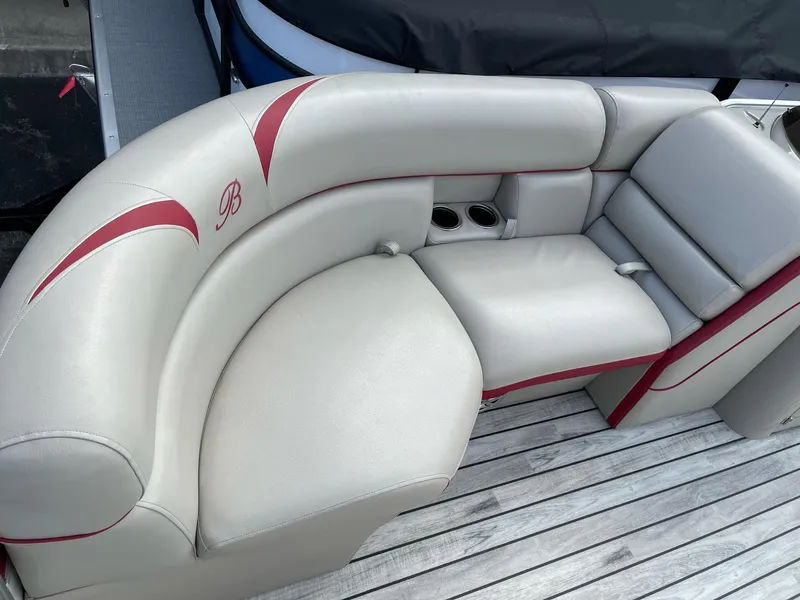 Slide: The Image of 2016 Berkshire 233RFX STS boat seating with beige upholstery and red accents on wooden deck. - 8