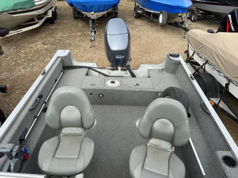 Slide: The Image of 2012 Alumacraft 165 Competitor boat with dual seats and motor, parked among covered boats. - 4