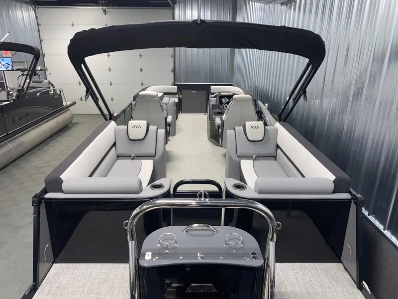 Slide: The Image of 2025 Avalon Catalina 2385 QL Tritoon boat with sleek interior and canopy in a showroom. - 2