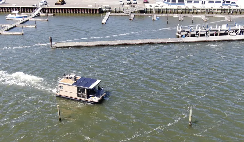 Slide: The Image of Aerial view of 2024 Waterlodge Apart M houseboat navigating a marina with docked boats. - 2