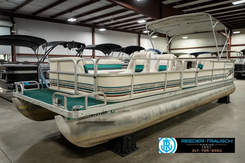 Slide: The Image of 1998 Odyssey 25 pontoon boat in indoor showroom, featuring green and white seating. - 3